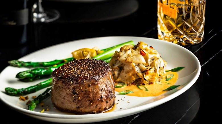 A white plate of steak, potatoes, and asparagus on a black table.