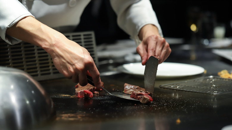 A chef cooking steak on a flat top.