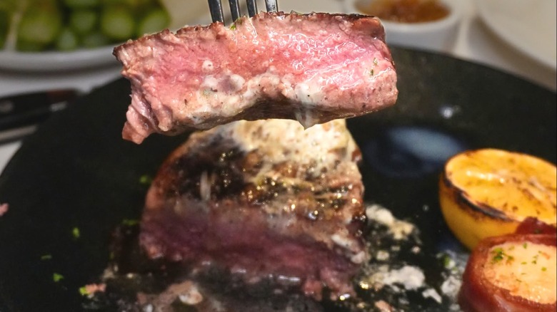 A fork lifting a buttery bite of steak from a black plate.