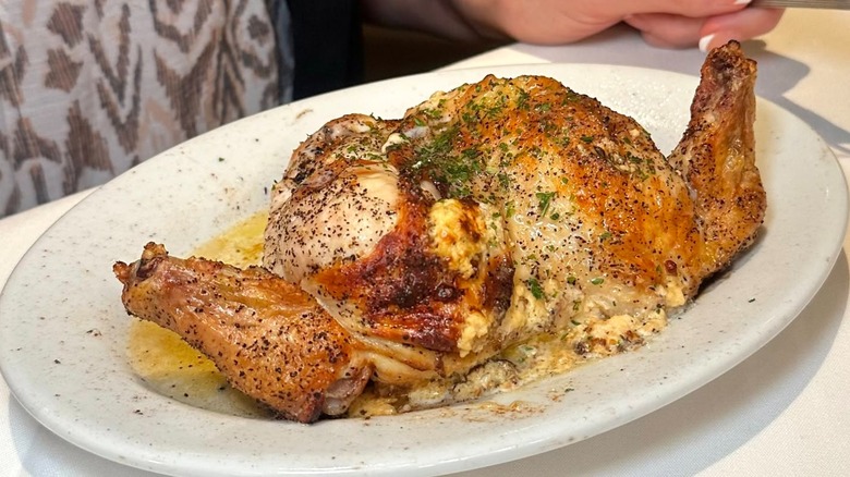 An oval white plate with a half roast chicken on it.