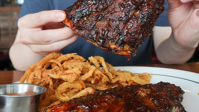 A man holding a rack of ribs above a full plate.
