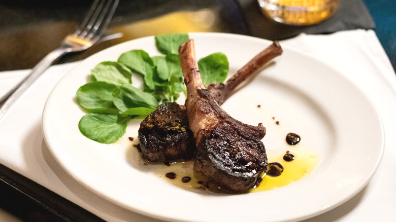 Two lamb chops positioned on a white plate with arugula and a drizzle of olive oil and balsamic vinegar.