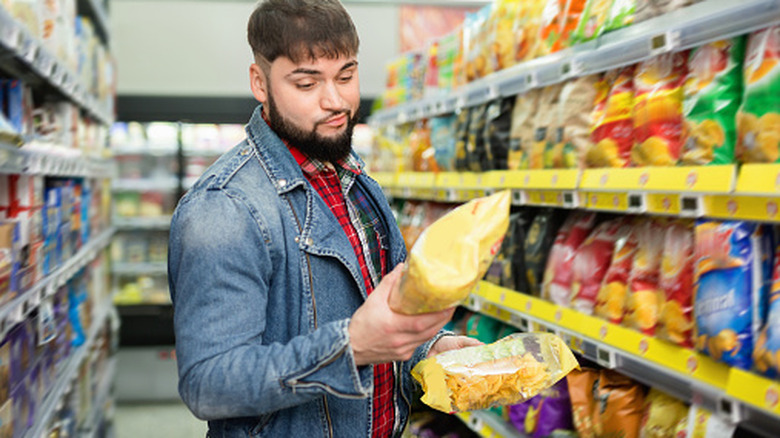 Man looking skeptically at bag of chips at grocery store