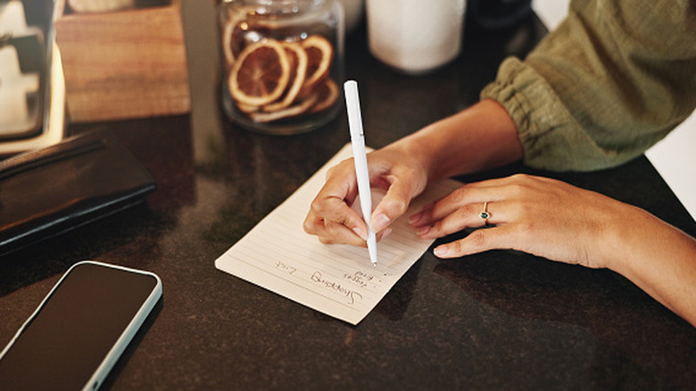 Hands writing a grocery shopping list on paper