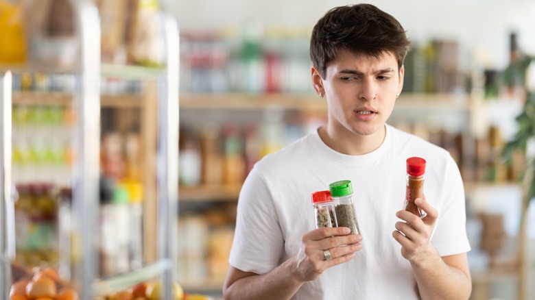 confused man holding three bottles of spices