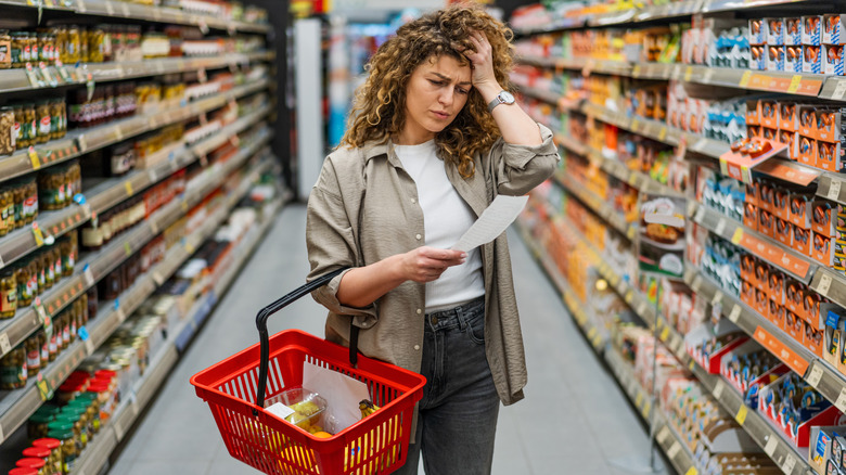 stressed woman looking at receipt in the middle of grocery store aisle