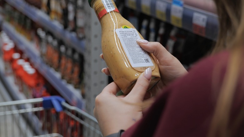Woman reading back of salad dressing bottle