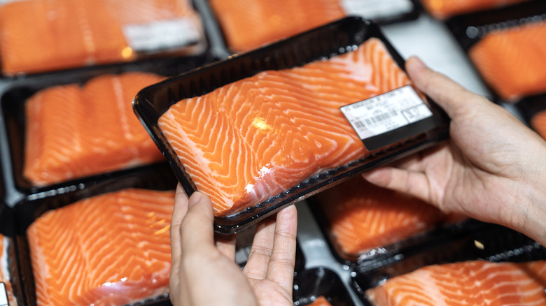 person holding packaged raw salmon at grocery store