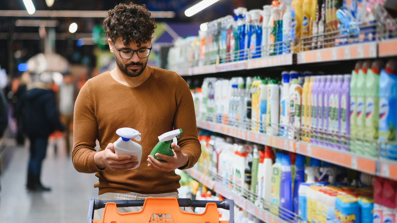 A man examining two spray bottles in the cleaning aisle of a supermarket