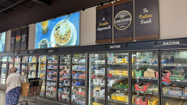 An aisle of Aldi refrigerated cases filled with their brand and a woman with a shopping cart