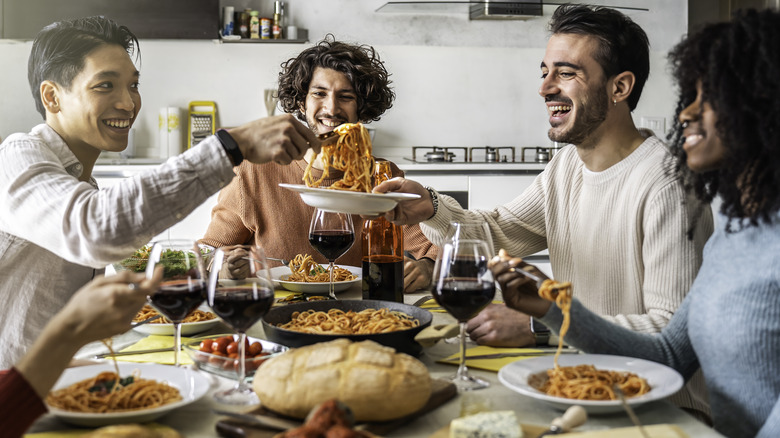 Friends eating spaghetti and drinking red wine together at home