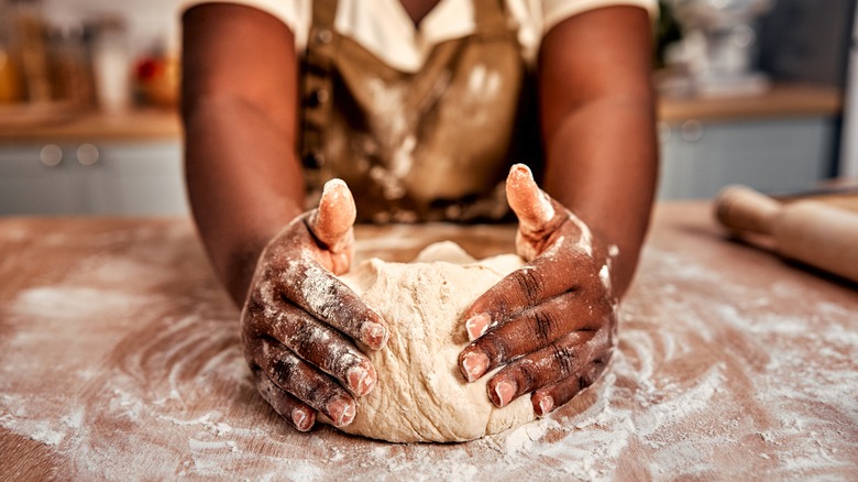 Baker's hands shaping bread dough on floured surface