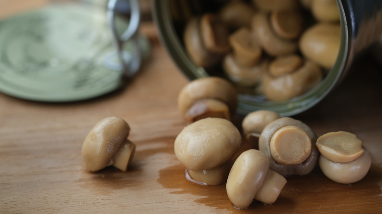 An open can of mushrooms lying on its side on a wood table.