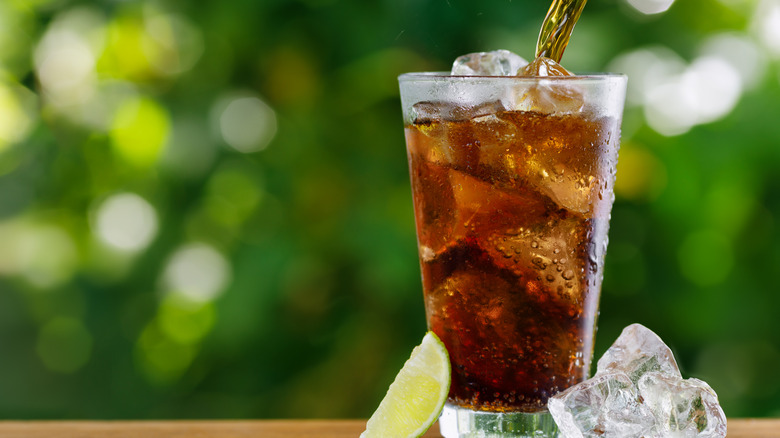 Someone pouring cola into an almost full glass.