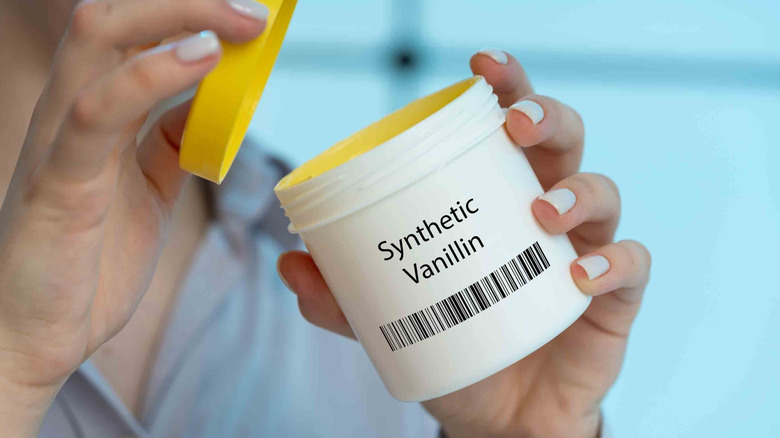 Hands opening a white jar labeled synthetic vanillin.
