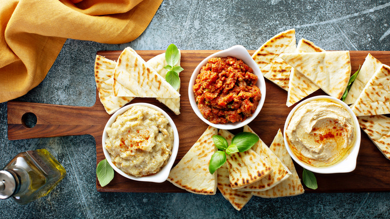 Hummus, dips, and grilled pita on a wood board