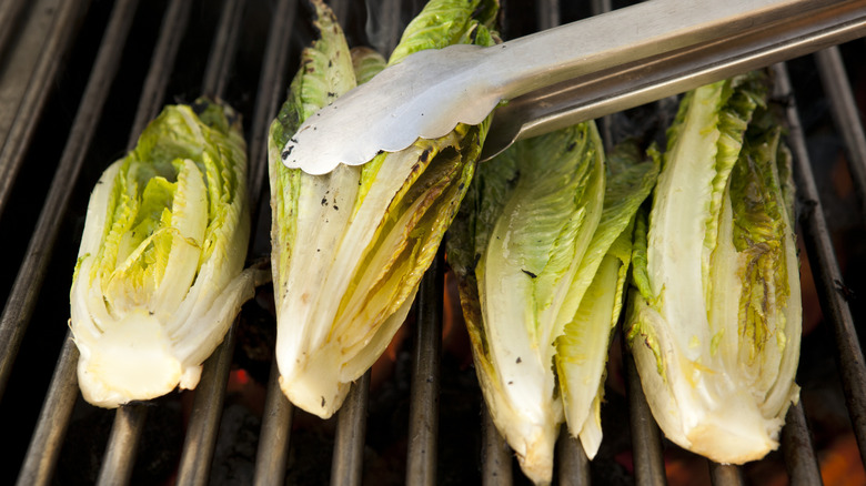 Four romaine hearts on a grill with metal tongs