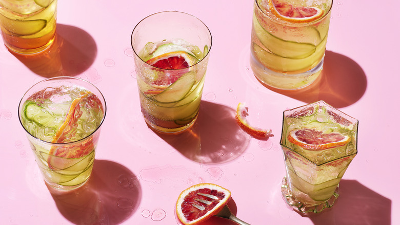 Five beverages with fruit in clear glasses with pink background