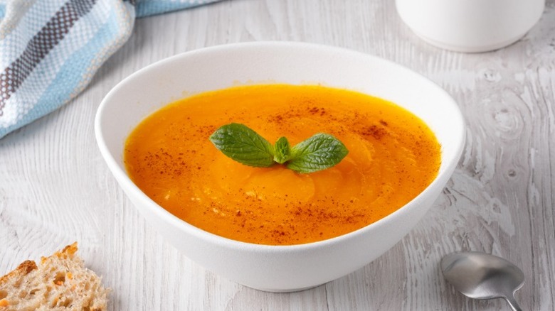 A bowl of orange soup with garnish on a tabletop
