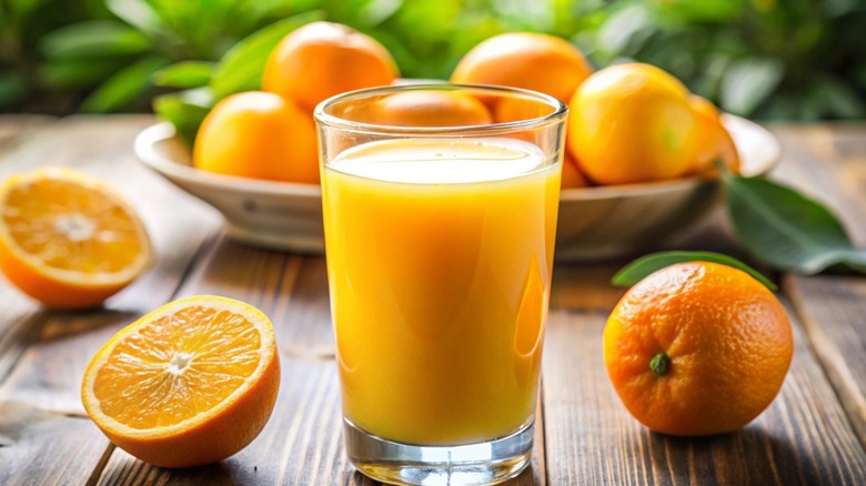 Cup of orange juice surrounded by sliced and whole oranges