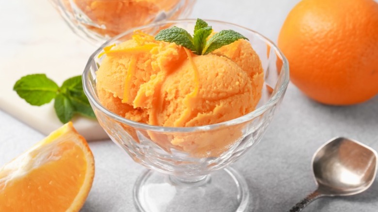 Cup of orange sorbet with spoon and whole oranges