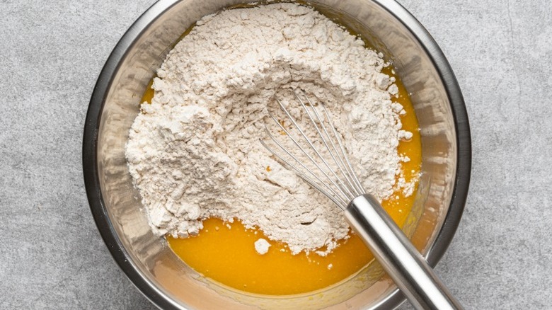 Boxed cake mix in bowl with egg yolks and whisk