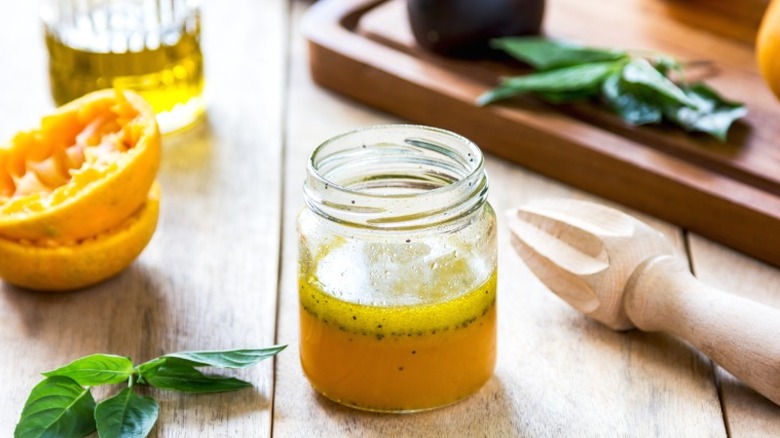 A mason jar filled with salad dressing with orange peels and herbs around it