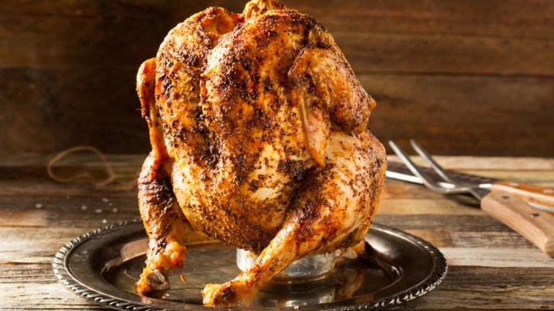 Whole chicken with beer can in cavity on wooden background