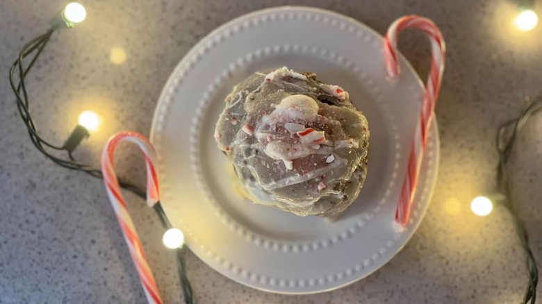 Cinnamon roll with crushed peppermint next to candy canes and Christmas lights
