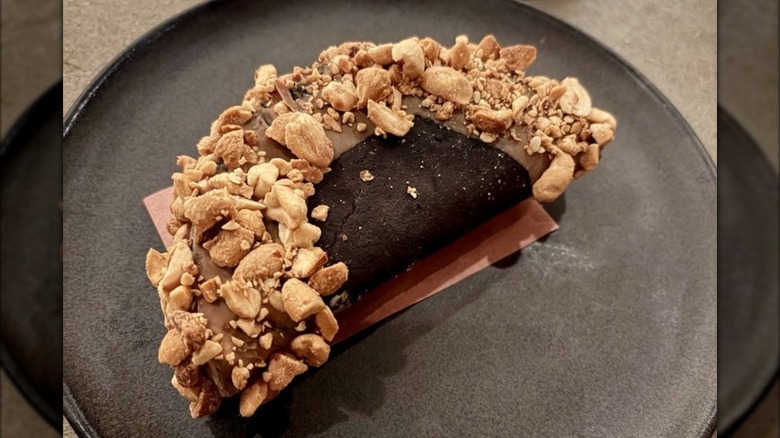 dessert taco with chocolate shell topped with nuts on a dark gray stoneware plate.