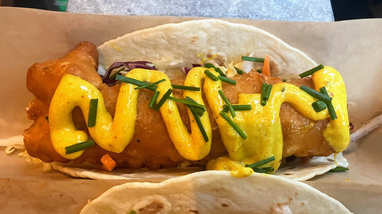 Close up of a fish taco topped with a yellow zig-zag drizzle of curry mayo