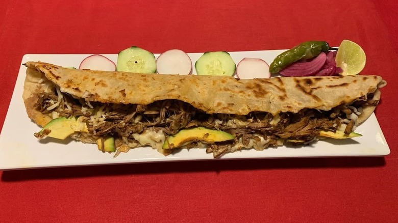 long Mexican quesadilla known as machete on an oblong plate with a row of cucumber and radish slices showing it's long size