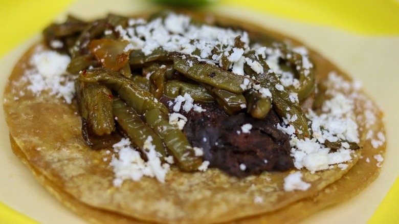 Corn tortilla filled with smooth black beans, strips of cactus, sprinkled with white, crumbly cheese