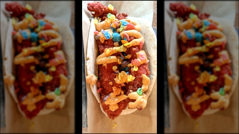 Closeup of a taco with red hot chicken strips, a drizzle of hot aioli, and a sprinkle of Fruity Pebbles cereal.