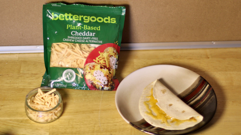 A bag of Bettergoods Plant-Based Cheddar cashew cheese beside a dish of the unbagged cheese and a small quesadilla on a plate