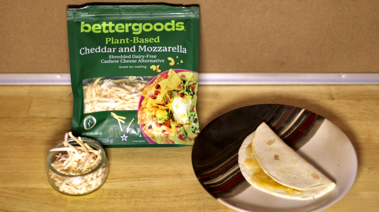 A bag of Bettergoods Plant-Based Cheddar and Mozzarella cashew cheese beside a dish of the unbagged cheese and a small quesadilla on a plate