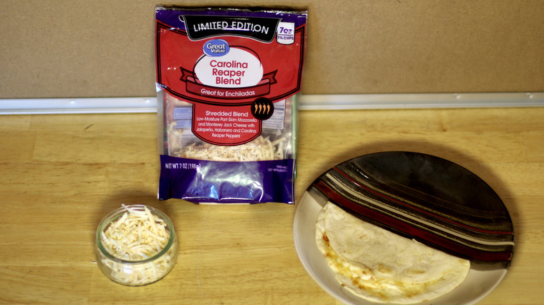A bag of Great Value Carolina Reaper Blend shredded cheese beside a dish of the unbagged cheese and a small quesadilla on a plate