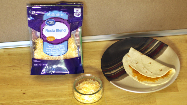 A bag of Great Value Fiesta blend shredded cheese beside a dish of the unbagged cheese and a small quesadilla on a plate
