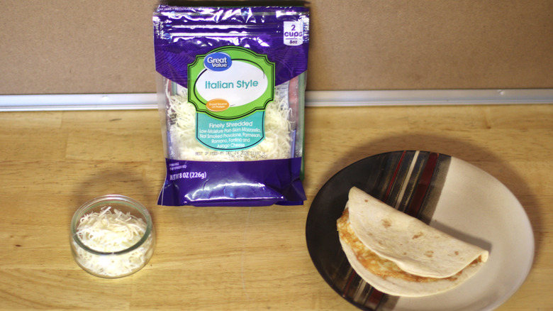 A bag of Great Value Italian Style shredded cheese beside a dish of the unbagged cheese and a small quesadilla on a plate
