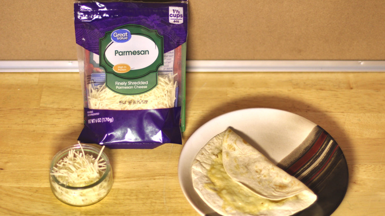 A bag of Great Value Parmesan shredded cheese beside a dish of the unbagged cheese and a small quesadilla on a plate