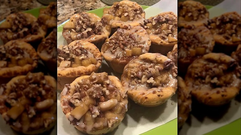 a plate of cinnamon roll cups filled with apples and topped with icing drizzle and pecans