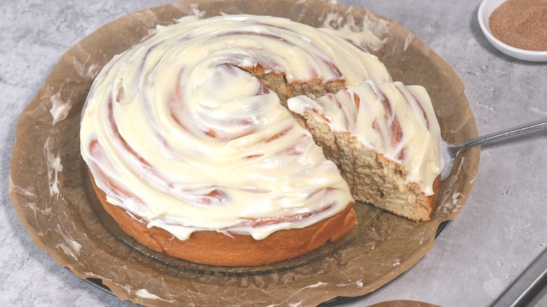 a giant cinnamon roll covered in icing with a slice being taken out of it