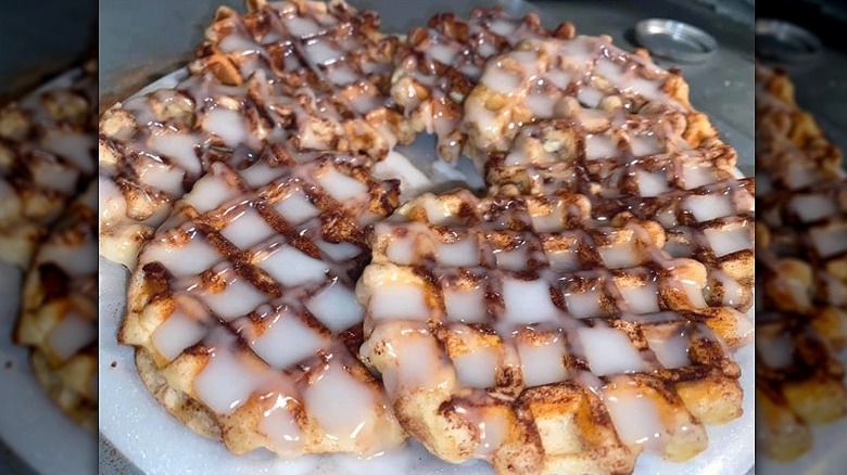 a plate of cinnamon roll waffles covered in a white glaze or icing