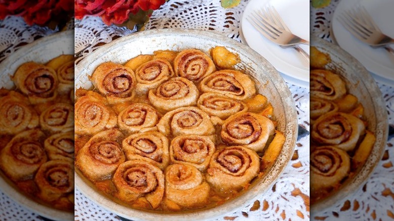 a peach cobbler topped with cinnamon rolls in a dish sitting on a white doily