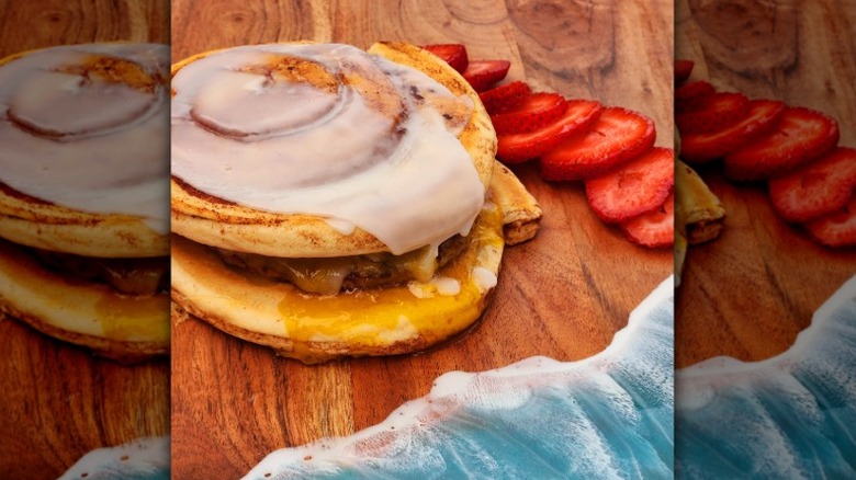 a breakfast sandwich with egg, cheese, and sausage on a cinnamon roll next to sliced strawberries
