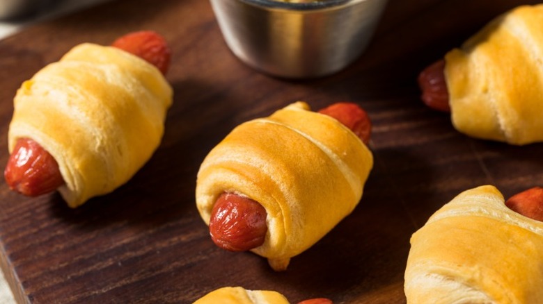 pigs in a blanket on a wooden board next to a sauce cup