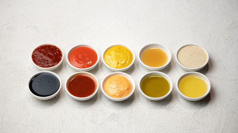 10 small dishes with different sauces on white background