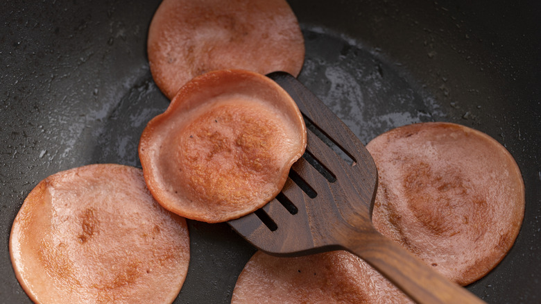 slices of bologna being flipped in frying pan
