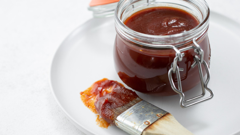 a mason jar of BBQ sauce with a basting brush on plate