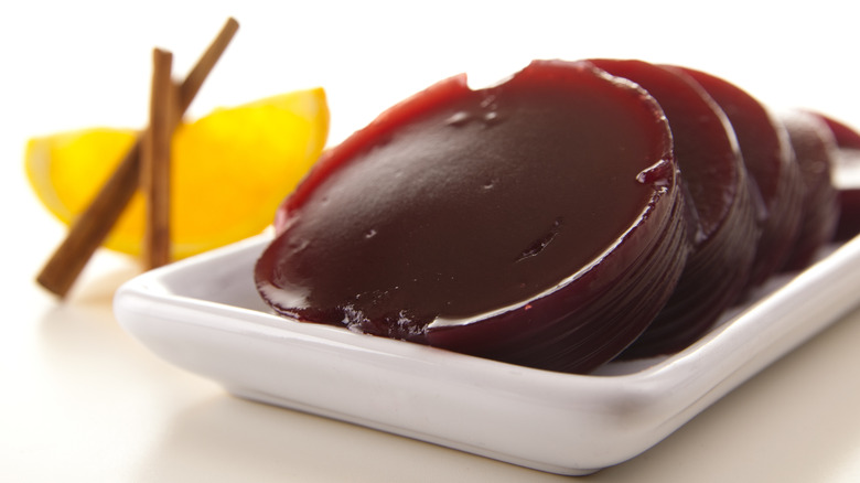 a plate with slices of canned jellied cranberry sauce with an orange wedge and cinnamon stick in the background